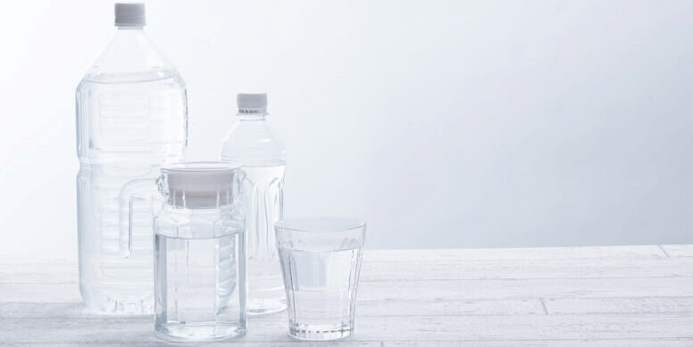 机の上に水が入った2本のペットボトルとピッチャーとグラスが並んでいる様子