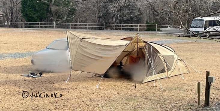 ogawaテント・シャンティRがキャンプ場の芝生の上で設営され、キャノピー部分を広げてタープのようにしている様子を100メートル位離れた場所から見た様子
