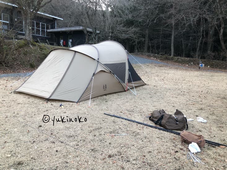 ogawaテント・シャンティRがキャンプ場の芝生の上に設営されており、手前にテントの袋、ペグ、キャノピーポールが無造作に置いてある