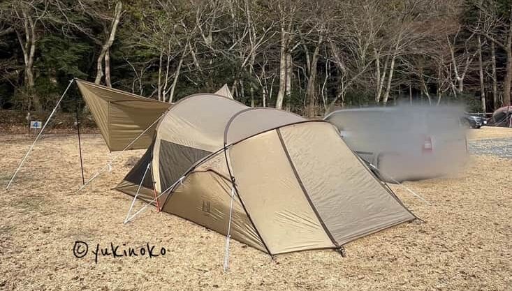 ogawaテント・シャンティRがキャンプ場の芝生の上で設営され、キャノピー部分を広げてタープのようにしている様子を後ろから見て左サイドの後ろから撮影したもの