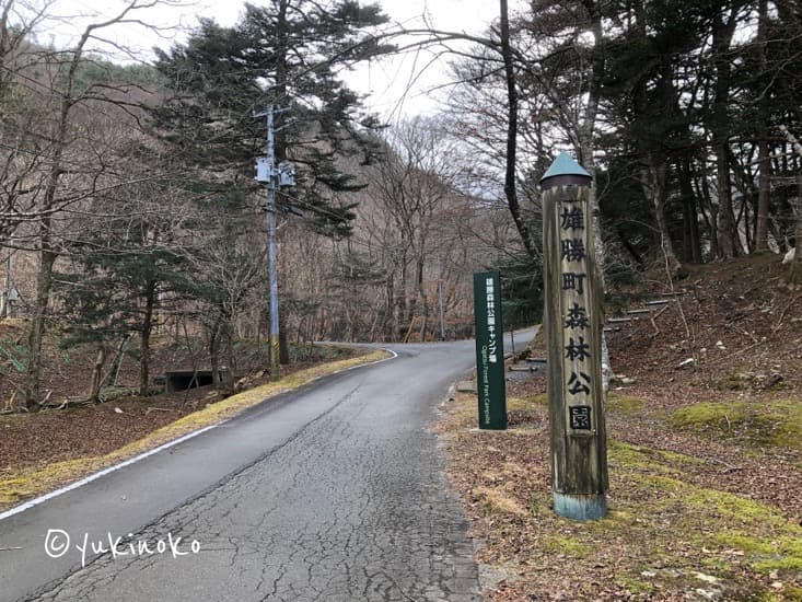 木で縦に長い看板に「雄勝町森林公園」と書かれていて、その看板が道路の右側に立っている