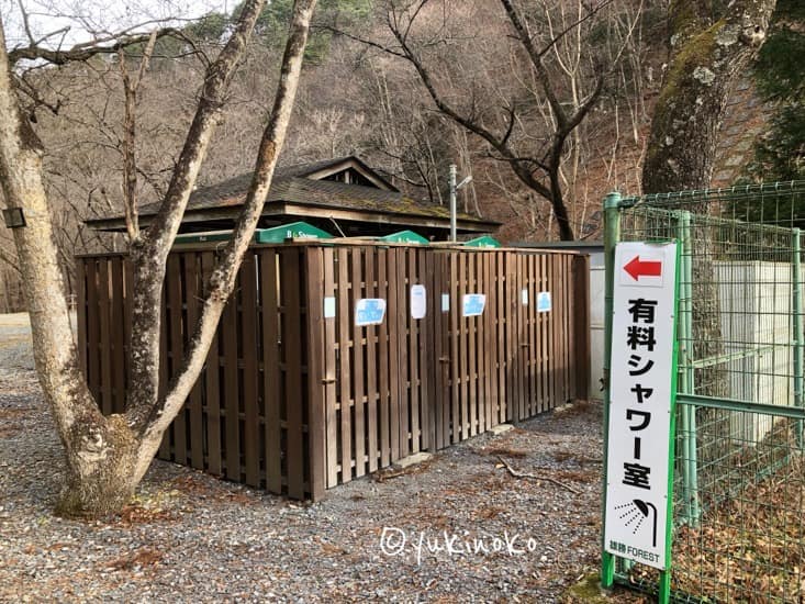 右手前に有料シャワー室と書かれた看板、左手前に木、中央に木の囲いに囲われたスペースが3つ隣り合って並んでいる