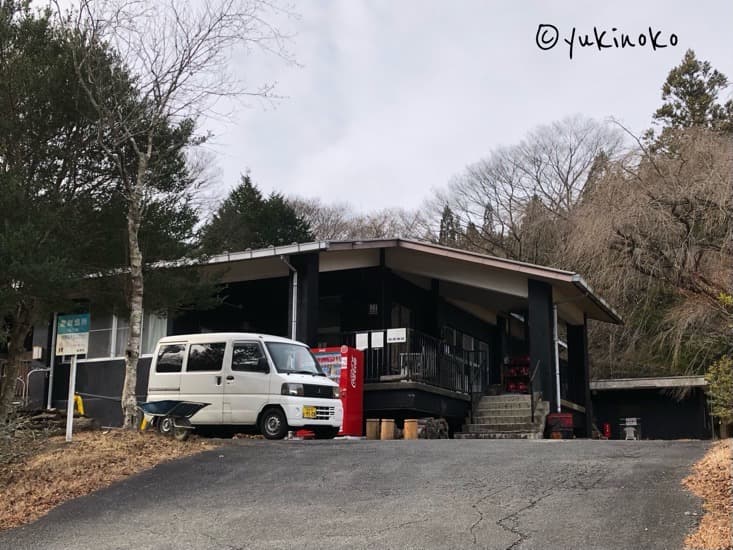 森林に囲まれた建物と、建物の手前には白い車と自販機がある