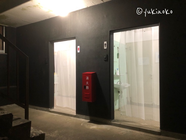 黒い壁の建物に入り口が二つあり、白い布製の半透明なカーテンがつけられている