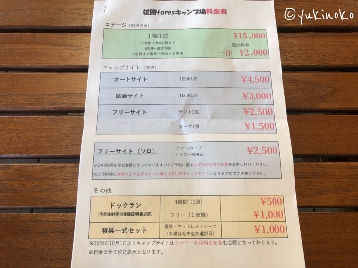 木のテーブルの上に、キャンプ場の料金表が記載された用紙が中央に置いてある