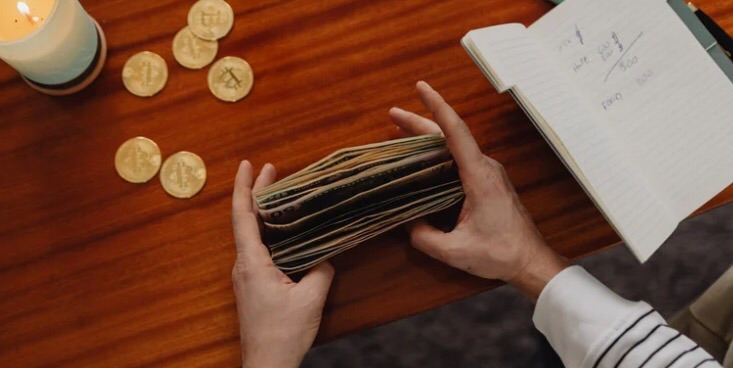 机上を上から見ていて、画像の左上にキャンドルとコイン6枚、右上にメモが書かれたノート、中央部分に両手でお札の束を整えている様子が写っている