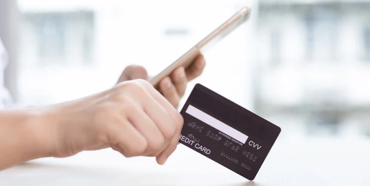 携帯を左手に、クレジットカードを右手に持って、テーブルの上で作業している様子をカード側の横から見た様子