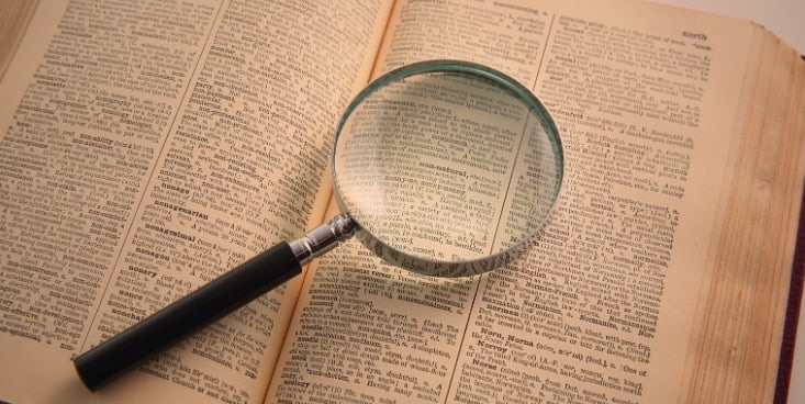 開いて置かれた辞書の上に虫眼鏡が置いてある