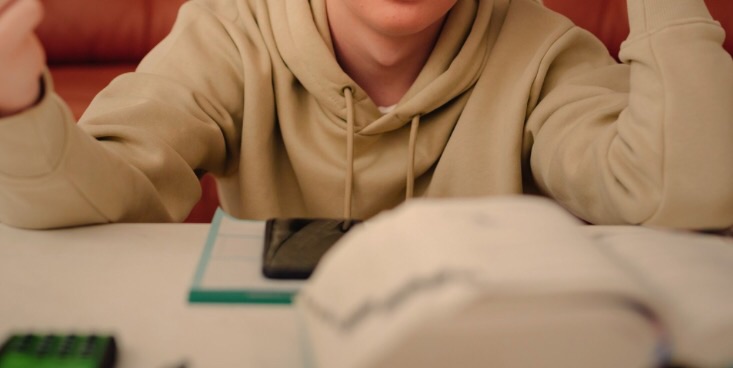 手前の机の上に辞書、ノート、携帯などが置いてあり、机に向かう形で奥に男性が考えている仕草で座って机に両肘をついている