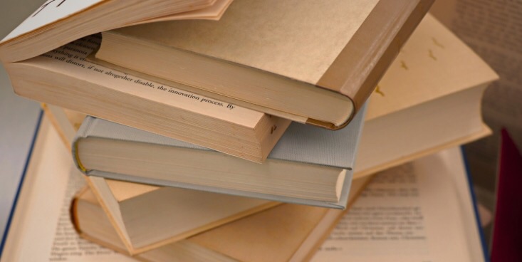 机の上に開いた本や本同士が挟まった本などが何冊も乱雑に積まれている